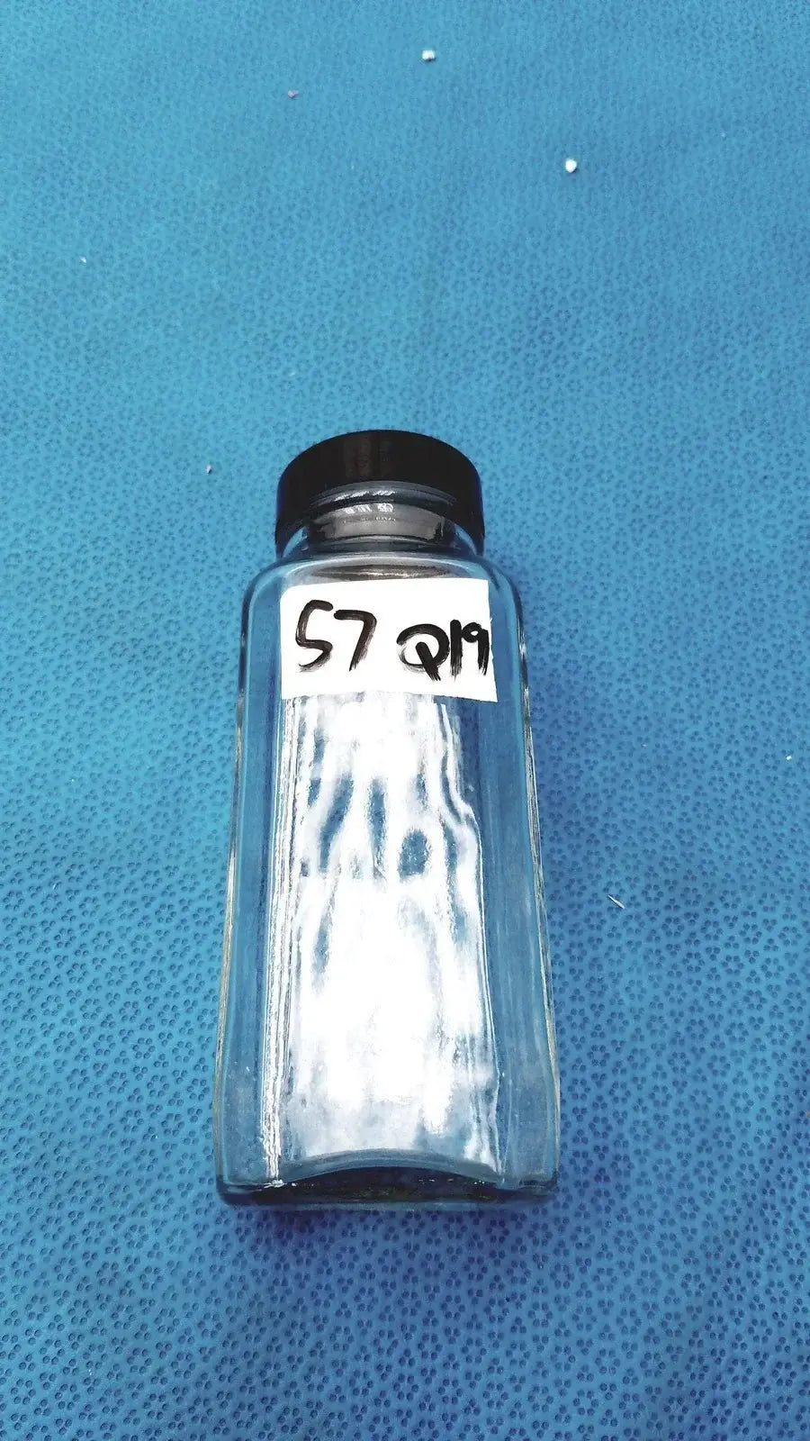 Square glass bottle with clear glass and black plastic lid labeled 57 q19 for reuse medical equipment or laboratory use