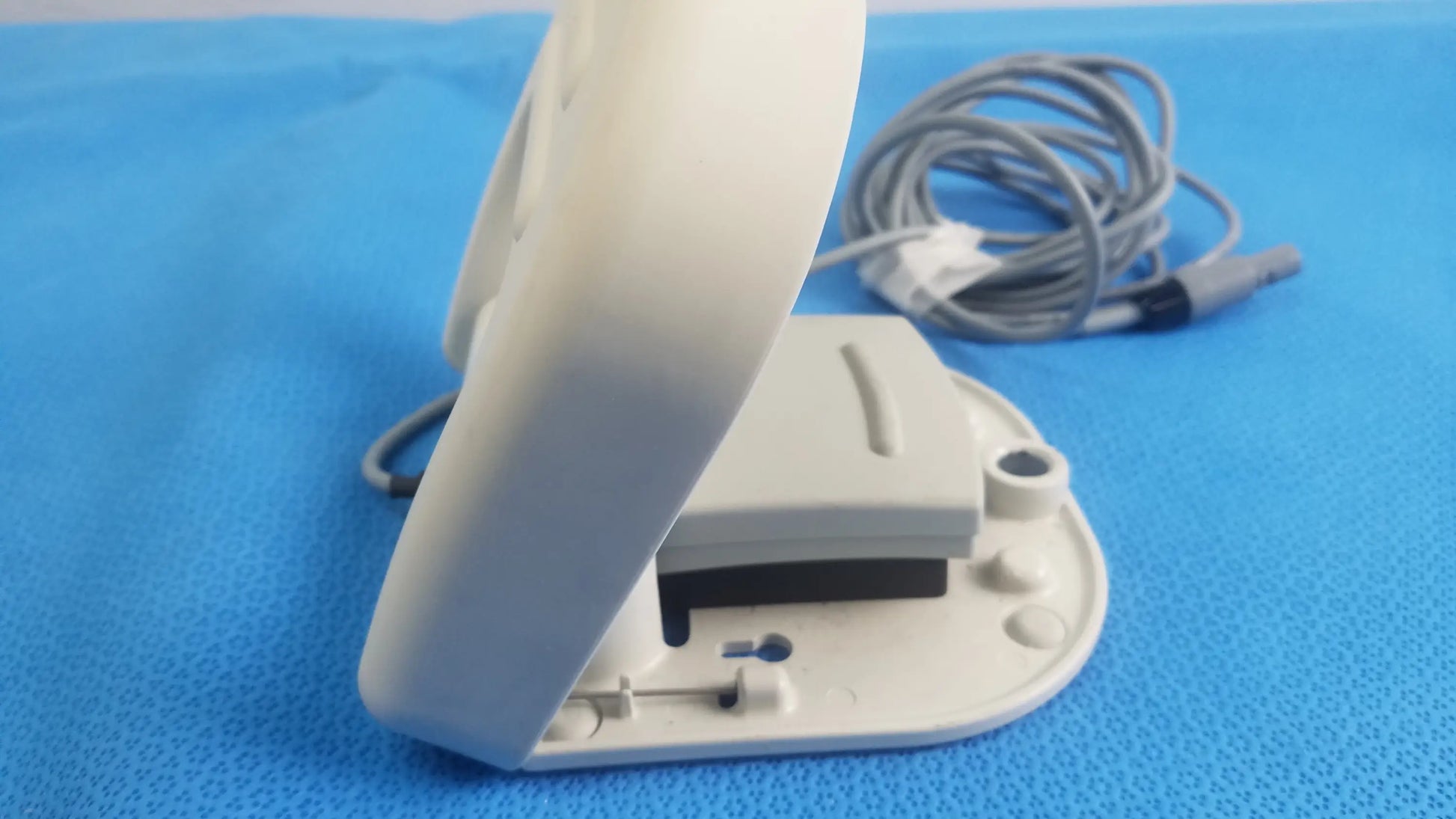 White plastic nintendo switch joy-con controller with coiled gray charging cable next to stokert smartablate foot pedal ref m490005 medical equipment