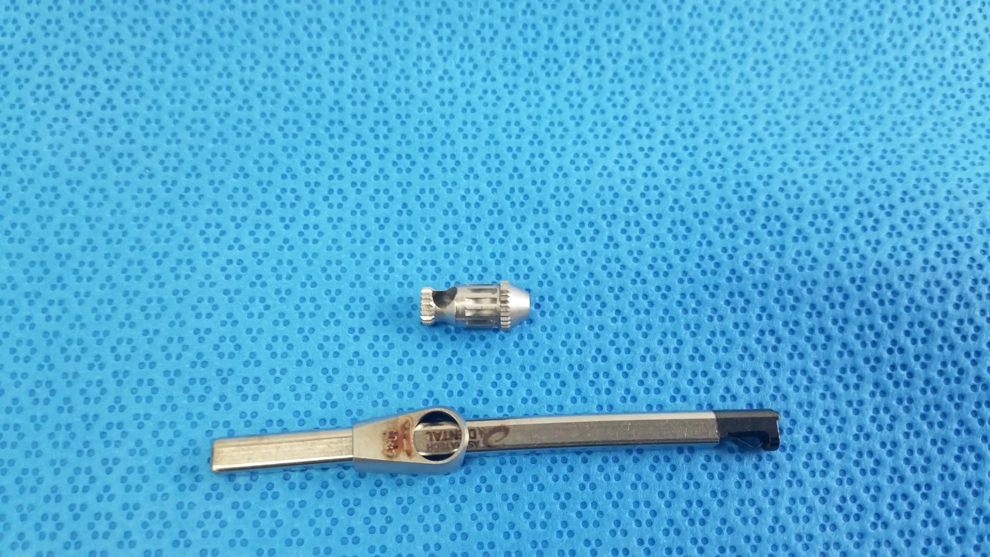 Silver metal valve stem cap with black handled tool included in straumann ultrasonic cleaning cassette for reuse medical equipment