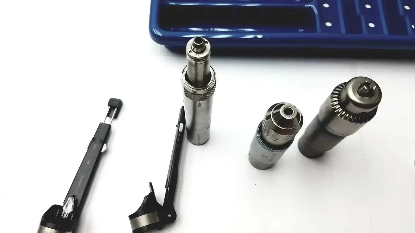 Silver metallic cylindrical tool bits with threaded ends and textured grips alongside precision instruments in a core sterilization case