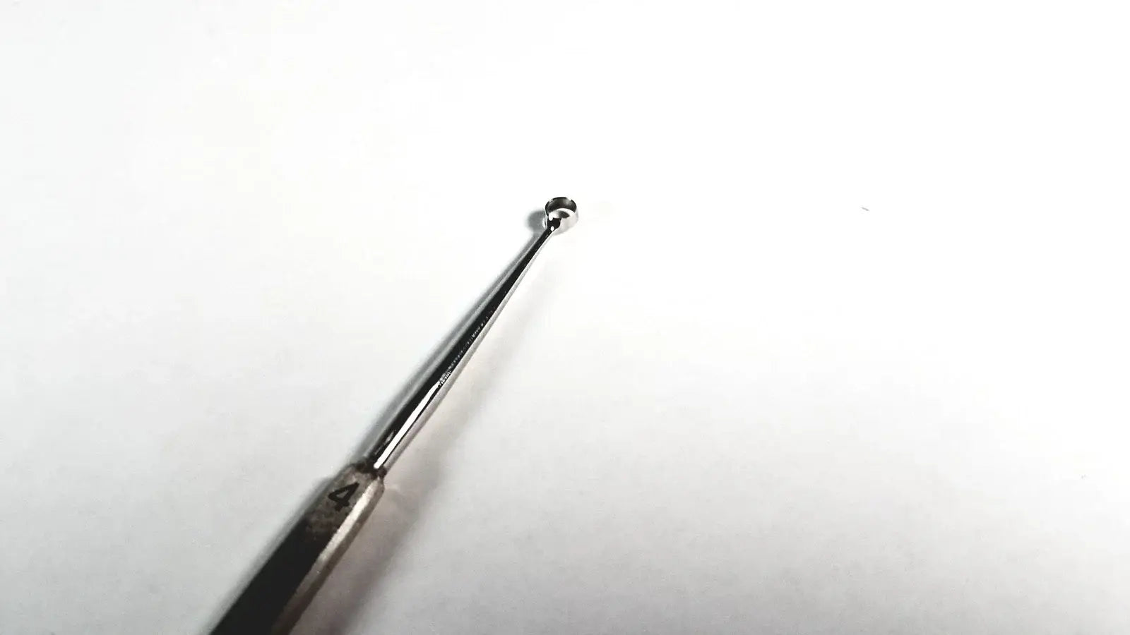 Silver-toned stainless steel tiemann surgical dermal curette size 4 with slender handle and small spherical tip medical equipment
