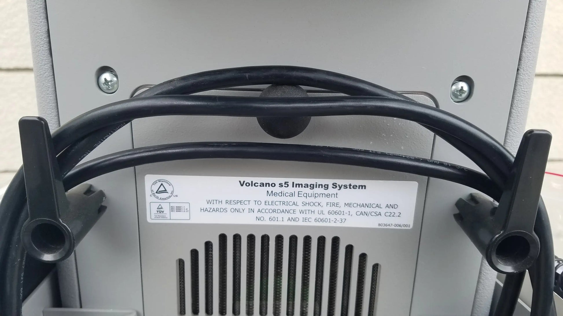 Black coiled cable with black plastic clamps securing it to the back of a gray Volcano S5 intravascular ultrasound medical equipment for reuse