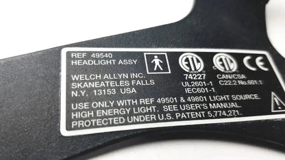 Black plastic label with white text and certification marks on the back of welch allyn 49540 surgical headlight assy