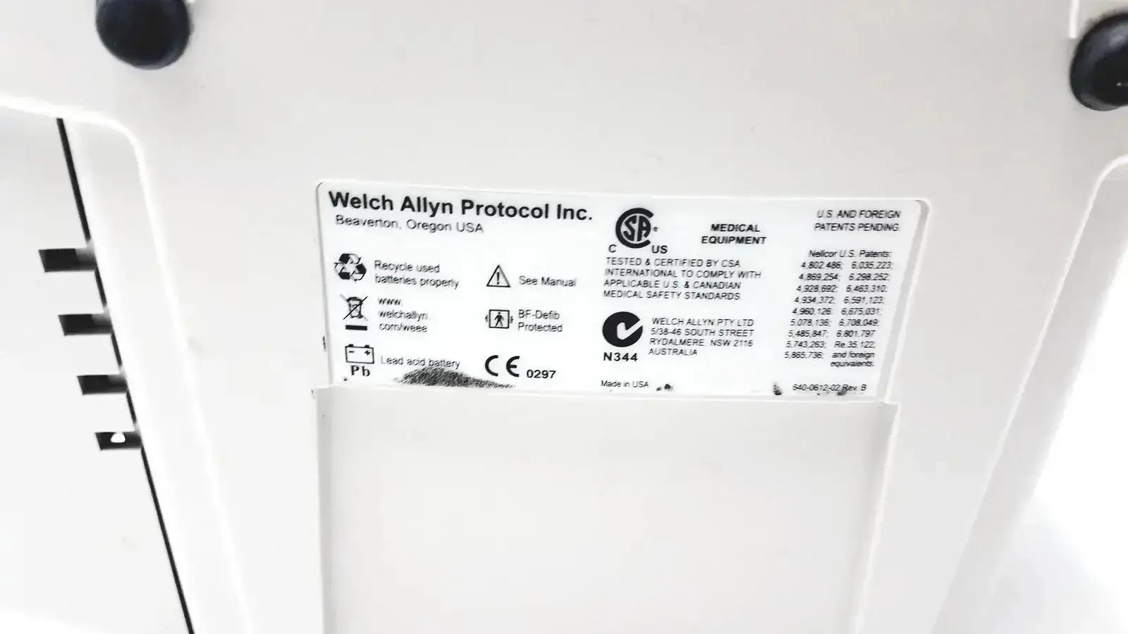 White plastic label with black text and symbols showing welch allyn protocol inc on welch allyn 530t0 patient monitor