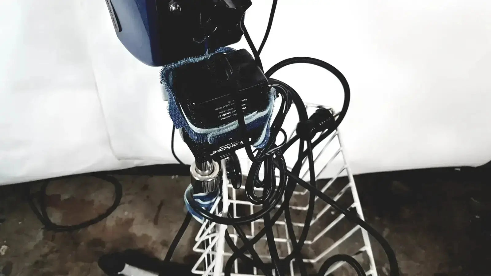 Blue and black welch allyn glidescope cobalt avl monitor with tangled wires resting on a white wire rack