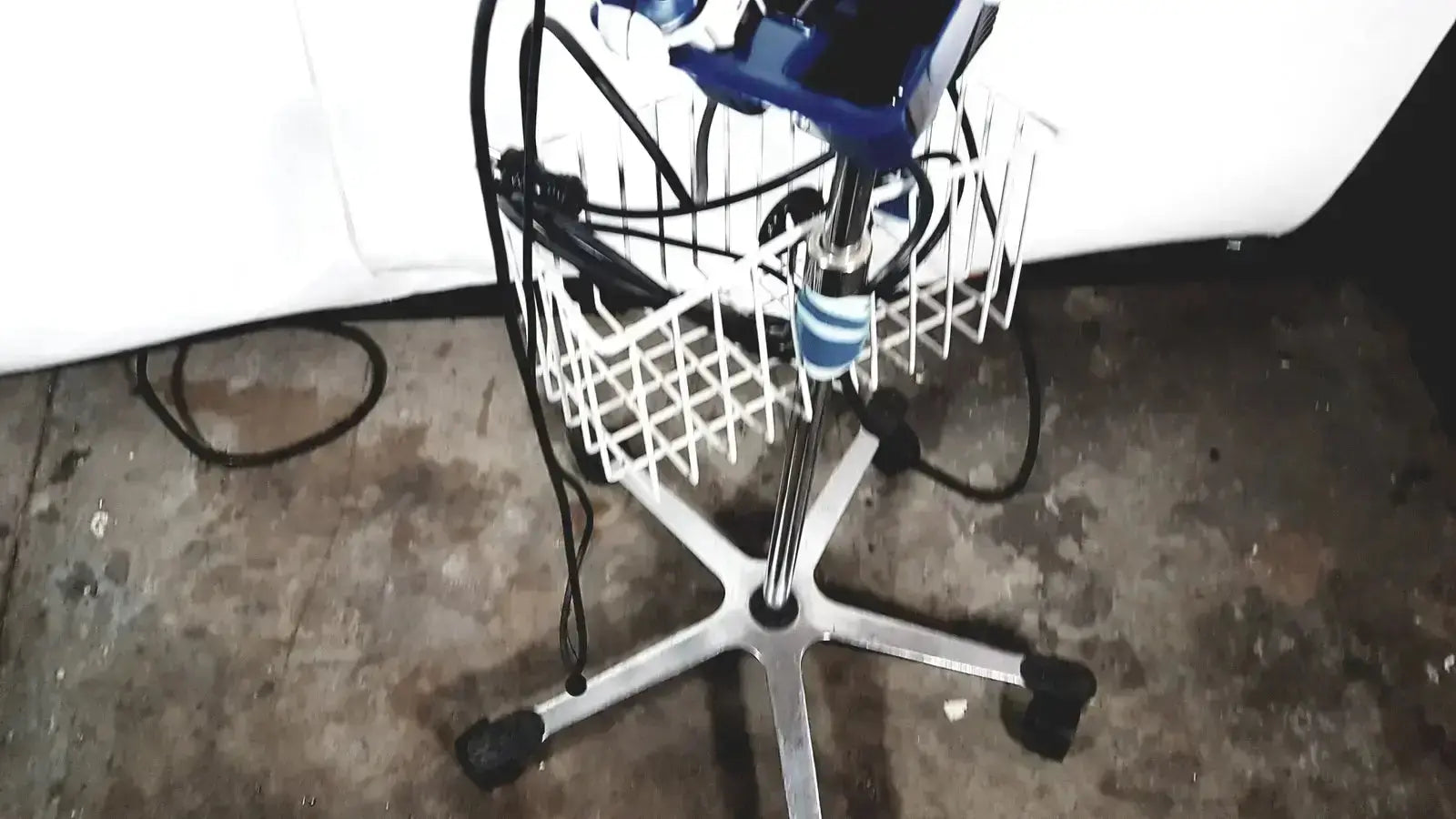 Blue and black electric hair dryer resting in white wire basket on office chair with chrome legs near welch allyn glidescope cobalt avl monitor