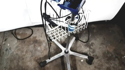 Blue and black electric hair dryer resting in white wire basket on office chair with chrome legs near welch allyn glidescope cobalt avl monitor
