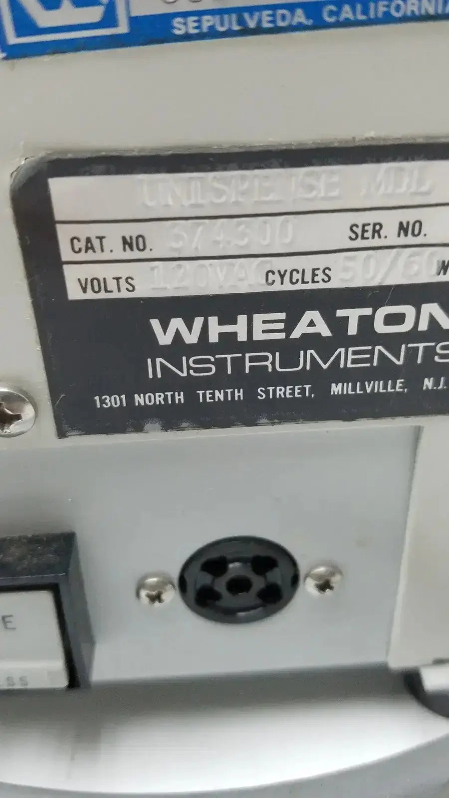 Gray wheaton instruments industrial equipment label with black text and blue logo showing unispense ii dose catalog number 374310