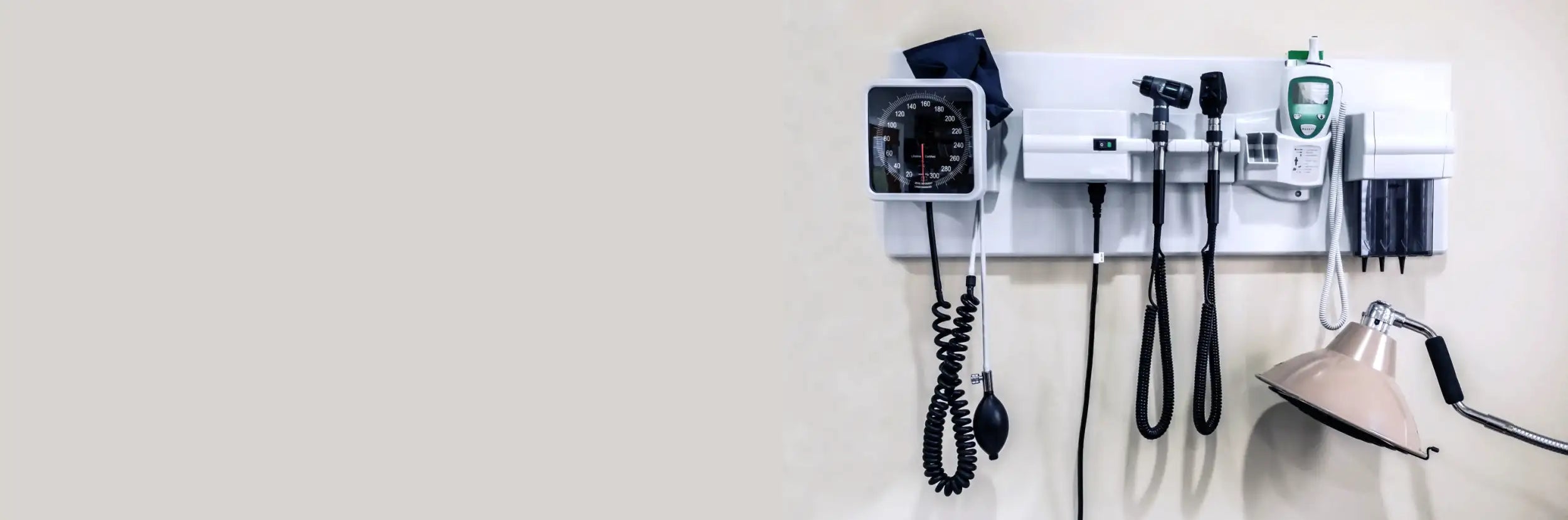 White wall-mounted medical equipment panel with black tubing and a green digital device