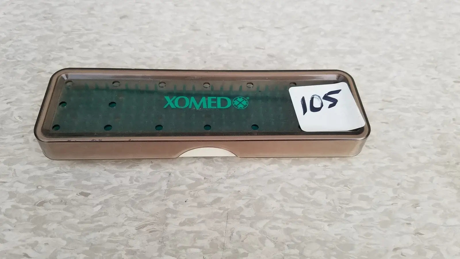 Brown plastic xomed poly vac dental instrument tray with green branding and circular holes for reuse medical equipment sterilization