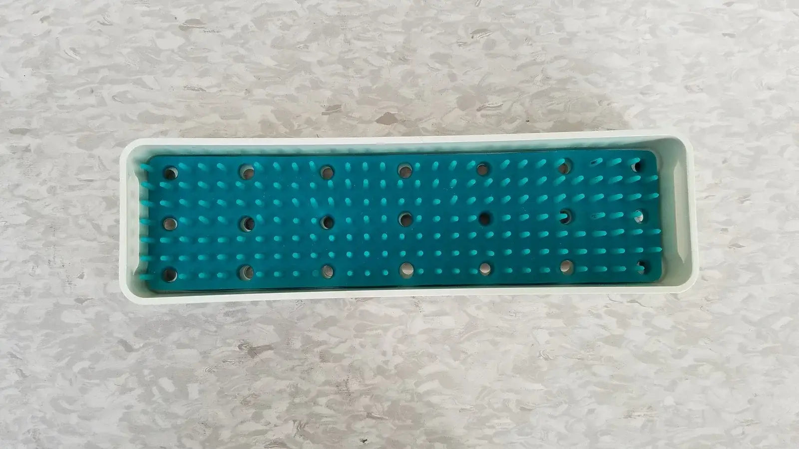 Teal silicone grip mat with white plastic frame and holes for xomed poly vac medical equipment sterilization case
