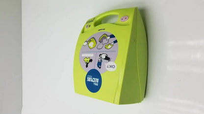 Lime green wall-mounted ZOLL AED Plus Trainer 2 case with handle and instructional diagrams for AED plus trainer use